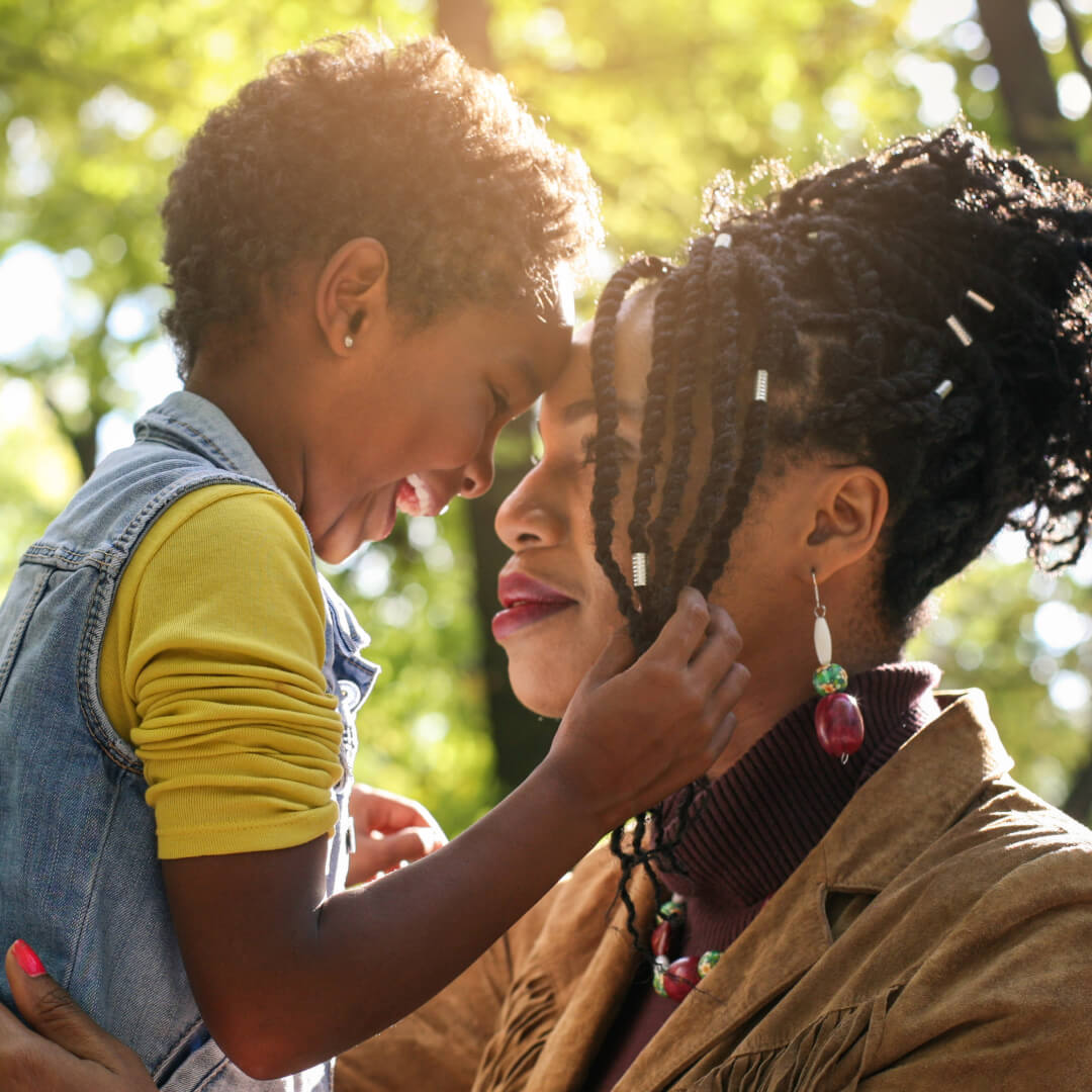 A BIPoC woman holds her child in a nature space