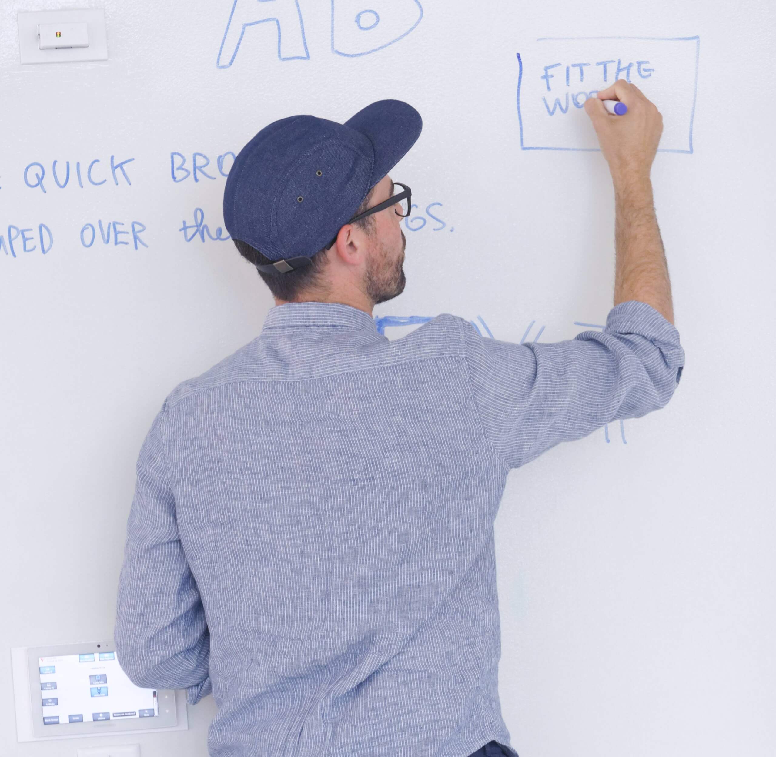A photo of a man with a baseball cap on writing on a whiteboard during a workshop at ID.