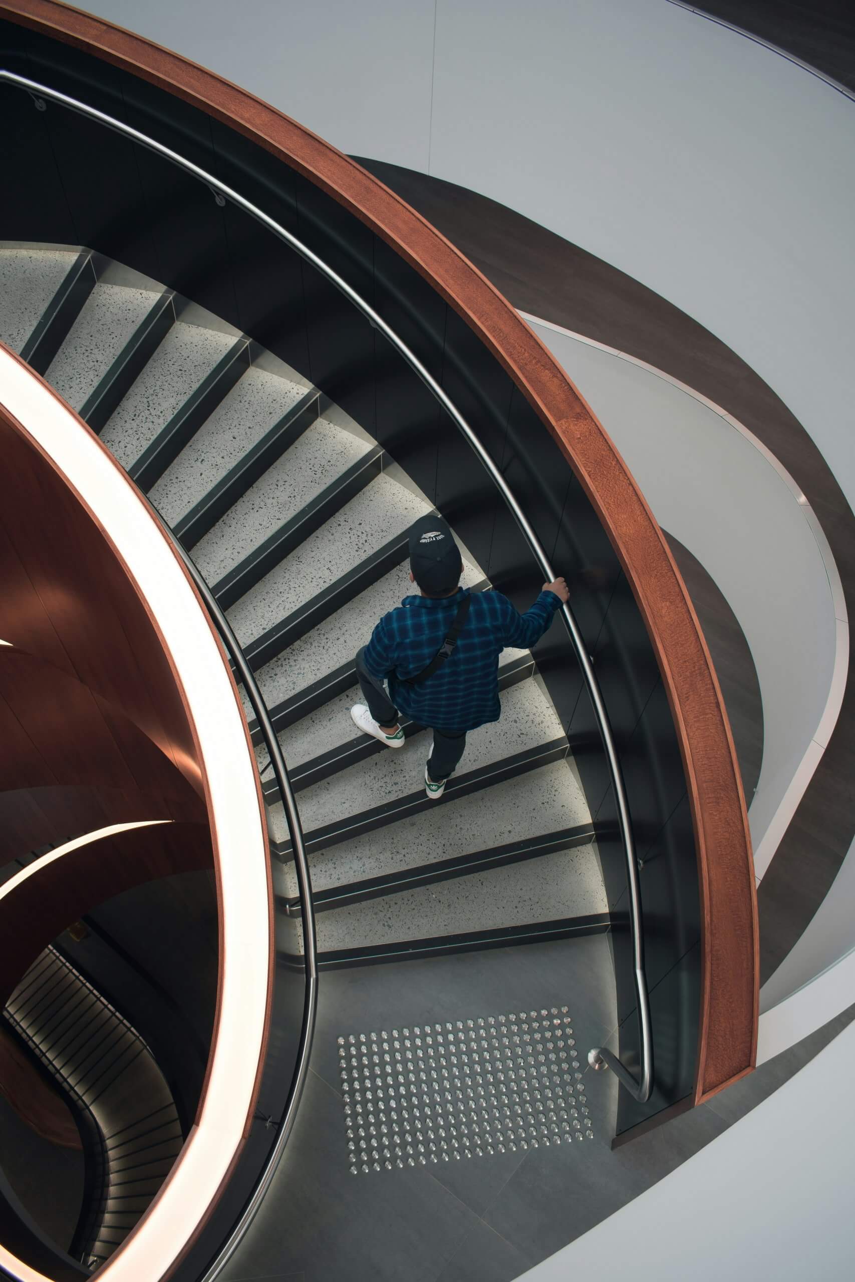 A photo of a man in a blue plaid shirt walking up a modern curved staircase.