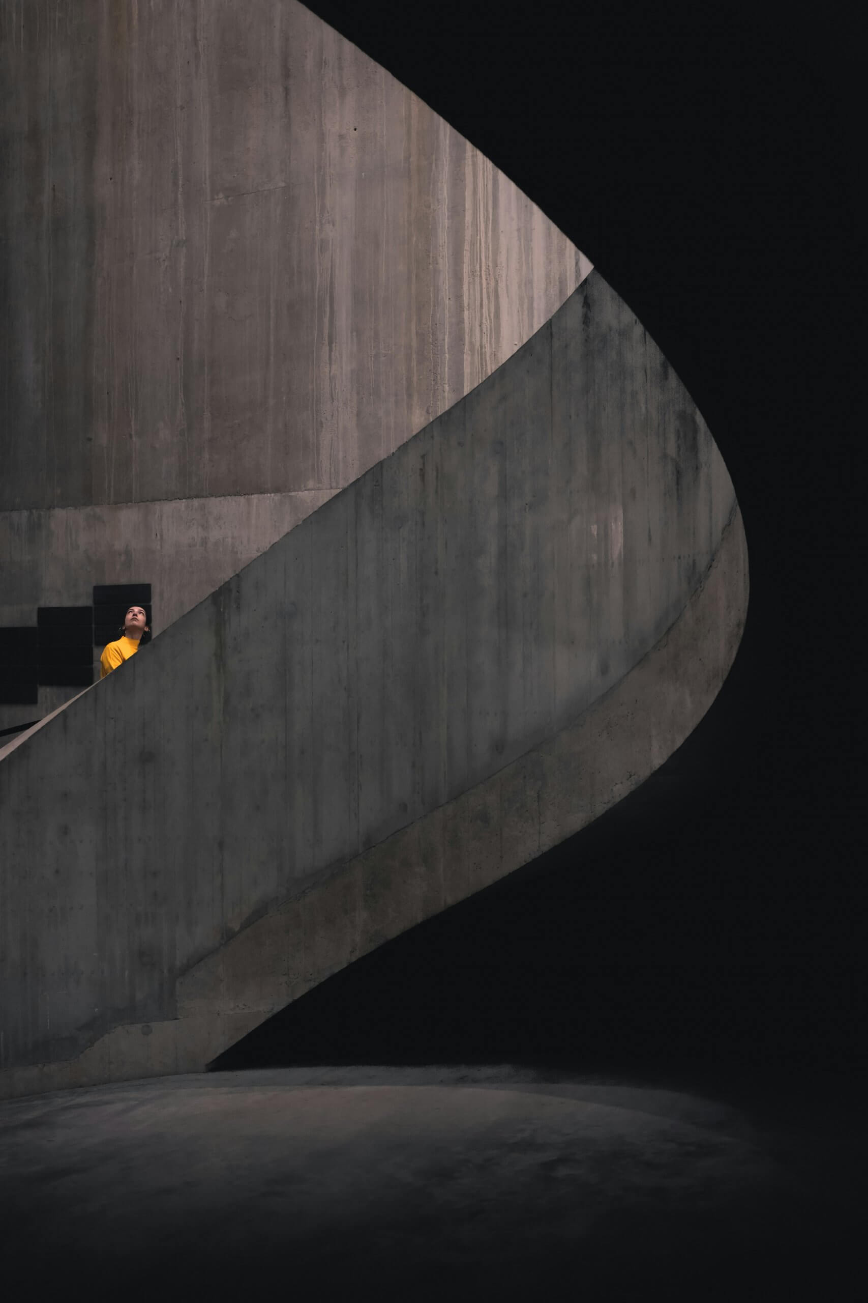 Photo of a man with a yellow shirt on a concrete, curved staircase.
